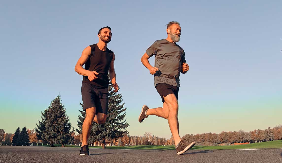 Vater und Sohn joggen auf der Strasse und lächeln.