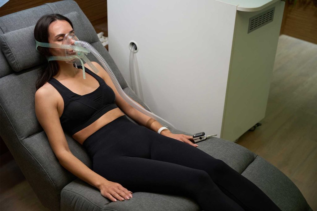 Frau liegt auf Couch im IHHT Zentrum Seevetal und atmet durch Sauerstoffmaske für das Höhentraining.