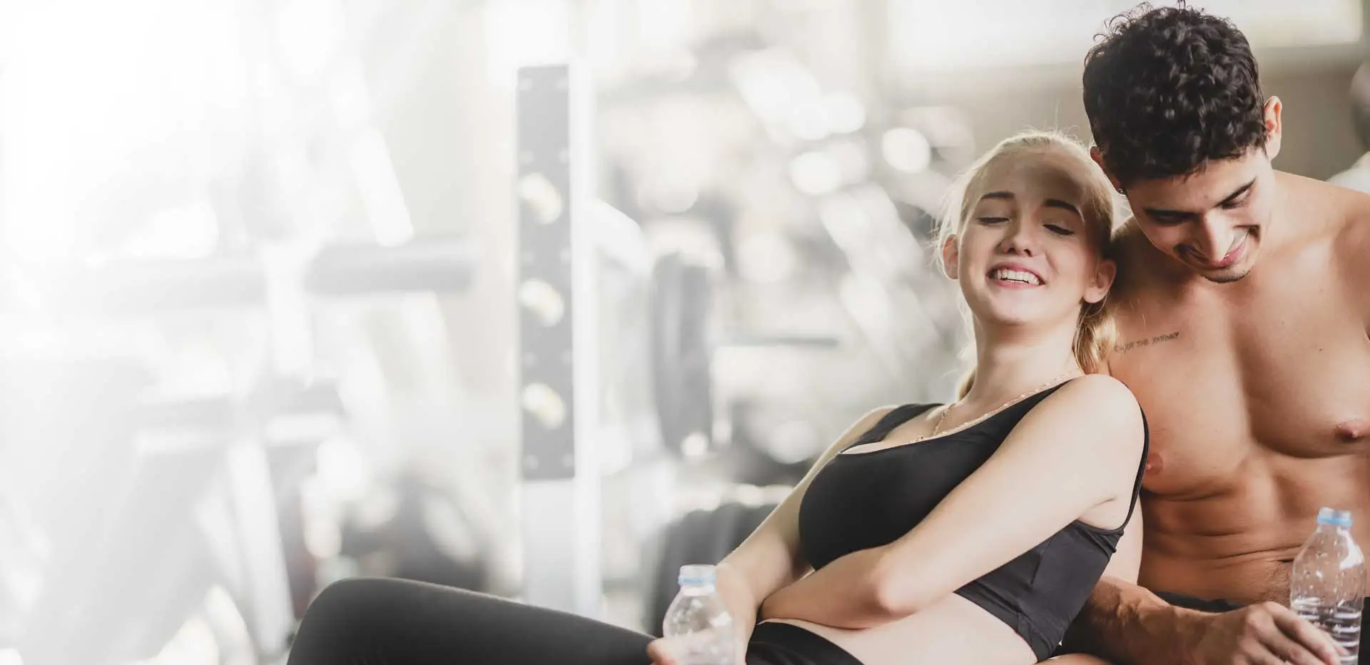 Junges Paar im Fitnesstudio machen Pause nach Höhentraining und trinken Wasser.