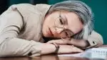 Frau leidet an Fatigue und schläft mit dem Kopf auf dem Tisch.
